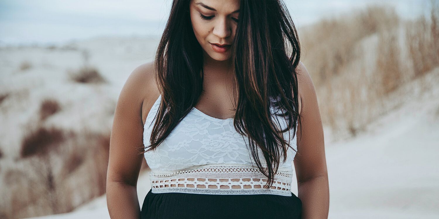 Pregnant woman standing on the beach with her hands around her bump