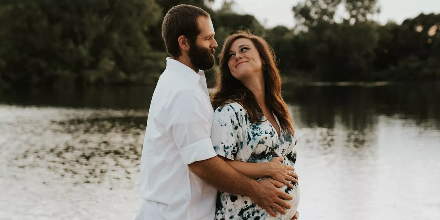 Een man omarmt de buik van een zwangere vrouw en lacht naar haar. 