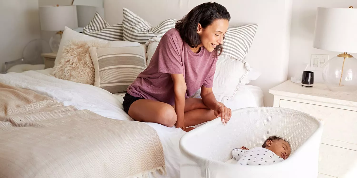 Mother lovingly looks into baby bed where her baby sleeps 