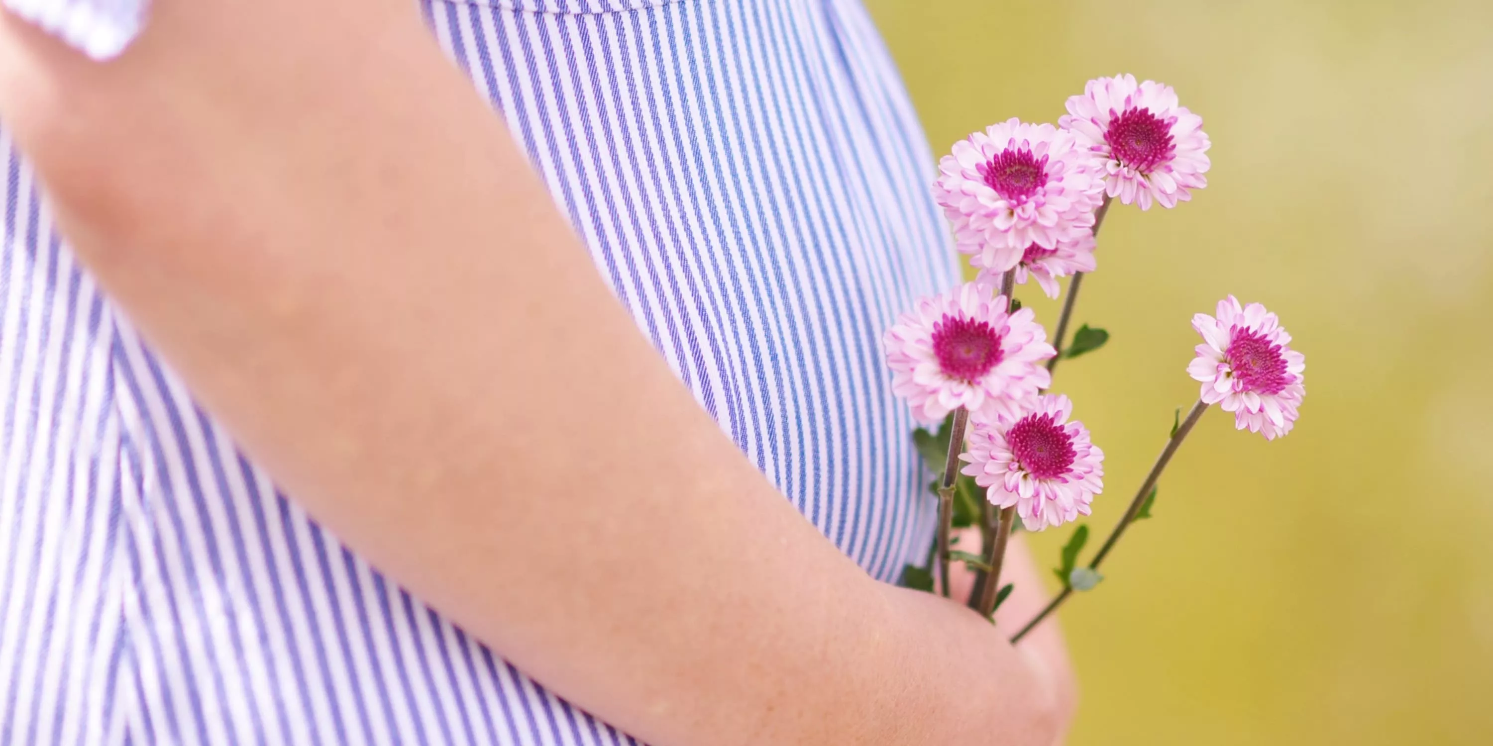 Een detailfoto van een babybuik van een zwangere vrouw die bloemetjes vasthoudt.