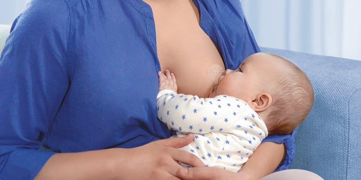 Junge Mutter stillt ihr Baby, während sie Stillhütchen trägt.