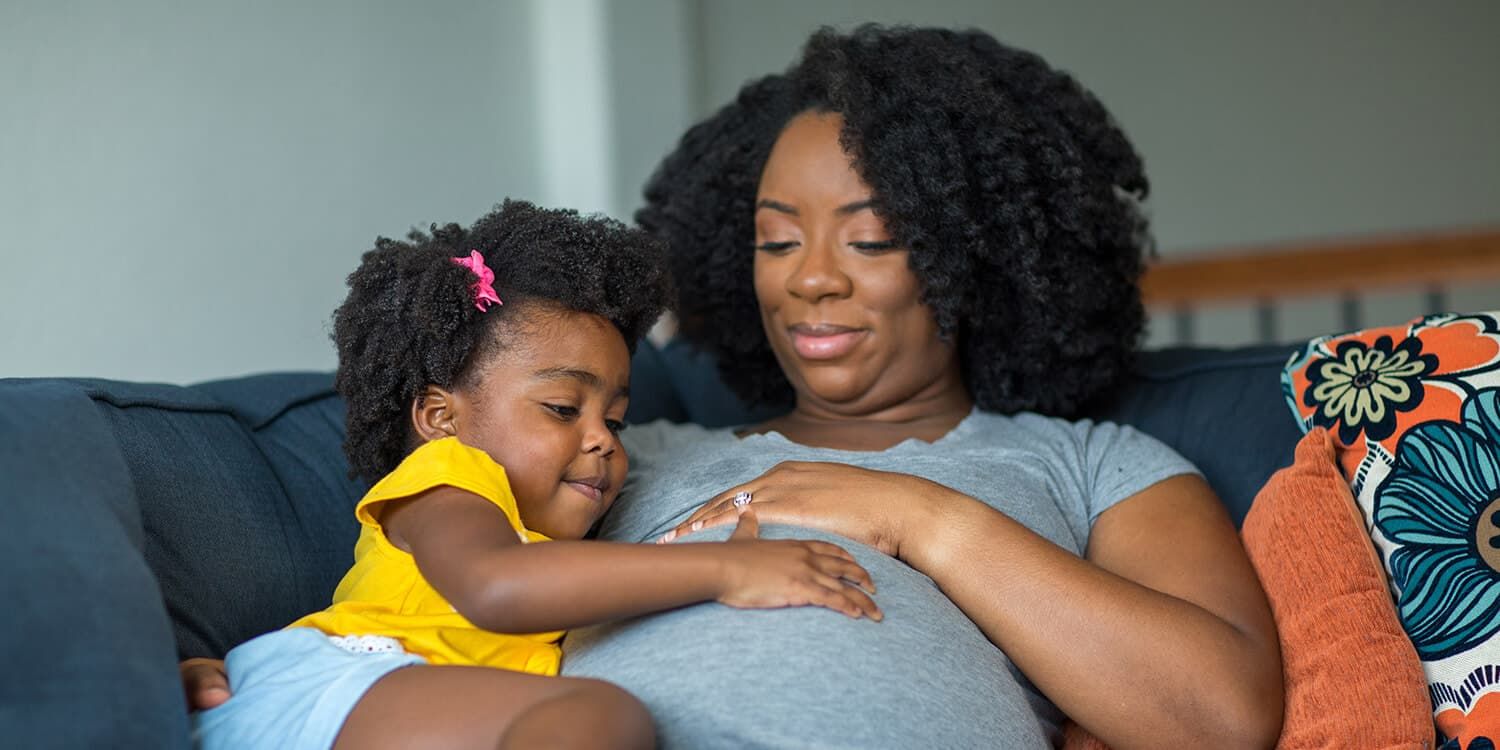 Uma menina coloca a mão na barriga da mãe grávida.