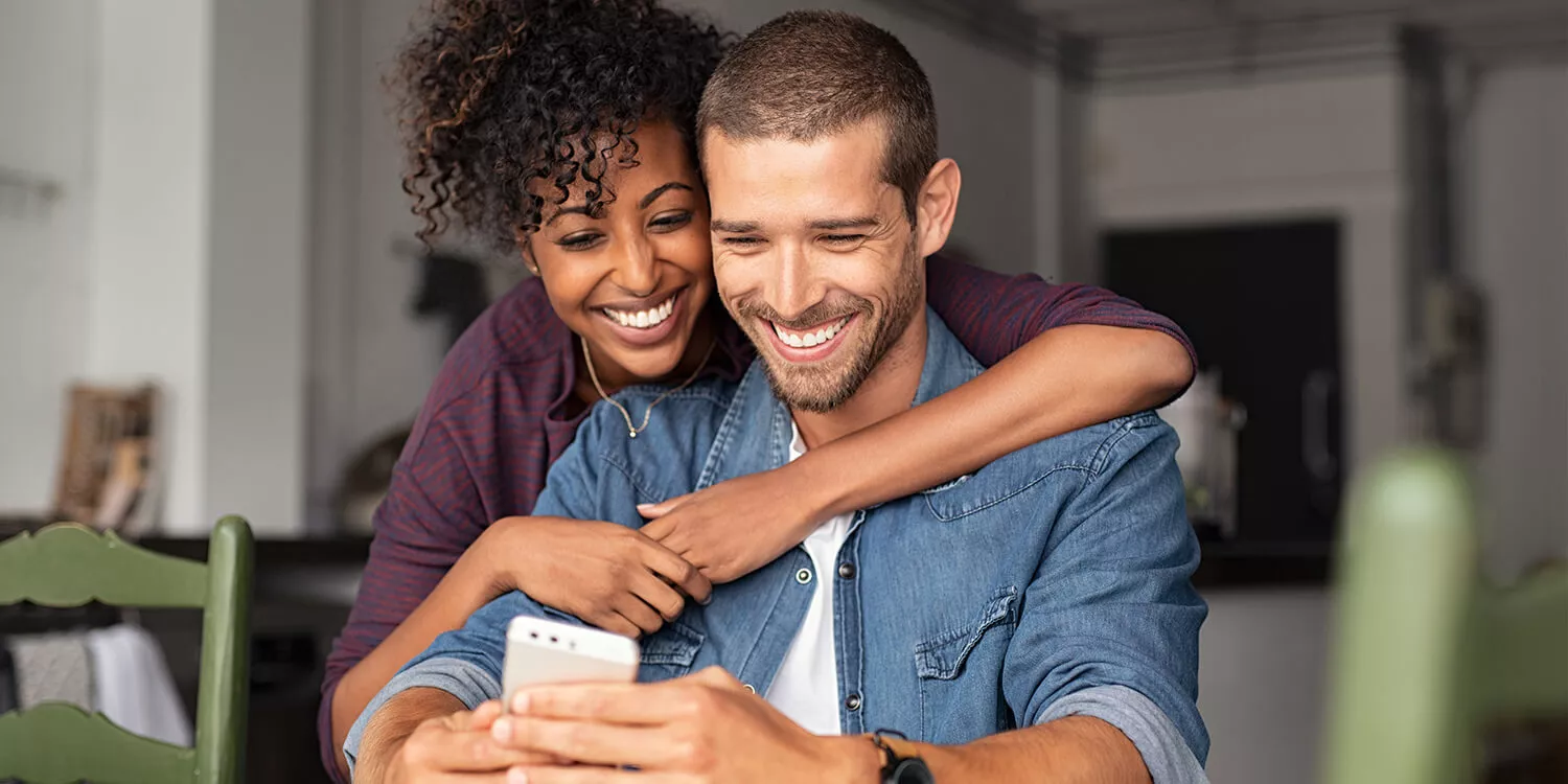Smiling young couple hugging each other while looking at a smartphone. 