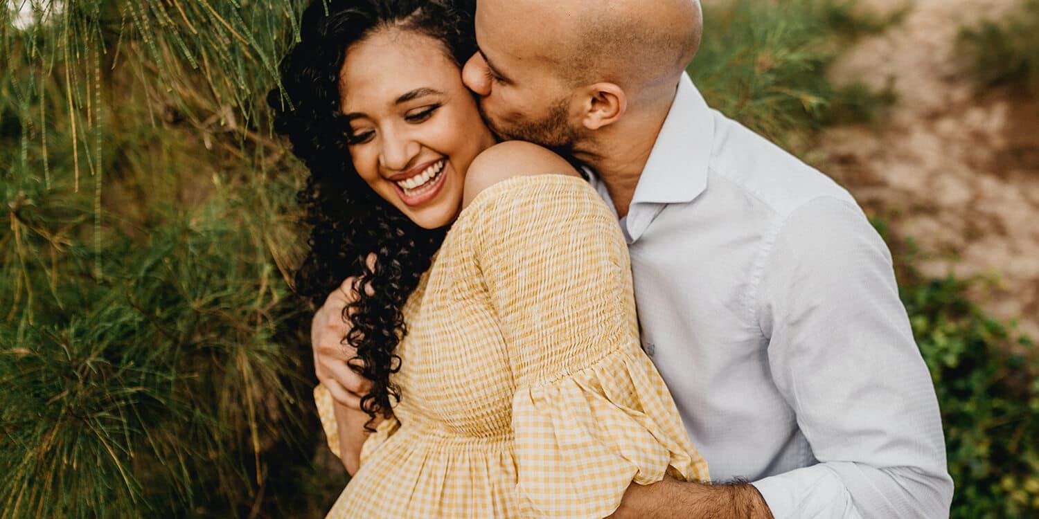Man cuddles pregnant woman and kisses her on the cheek 