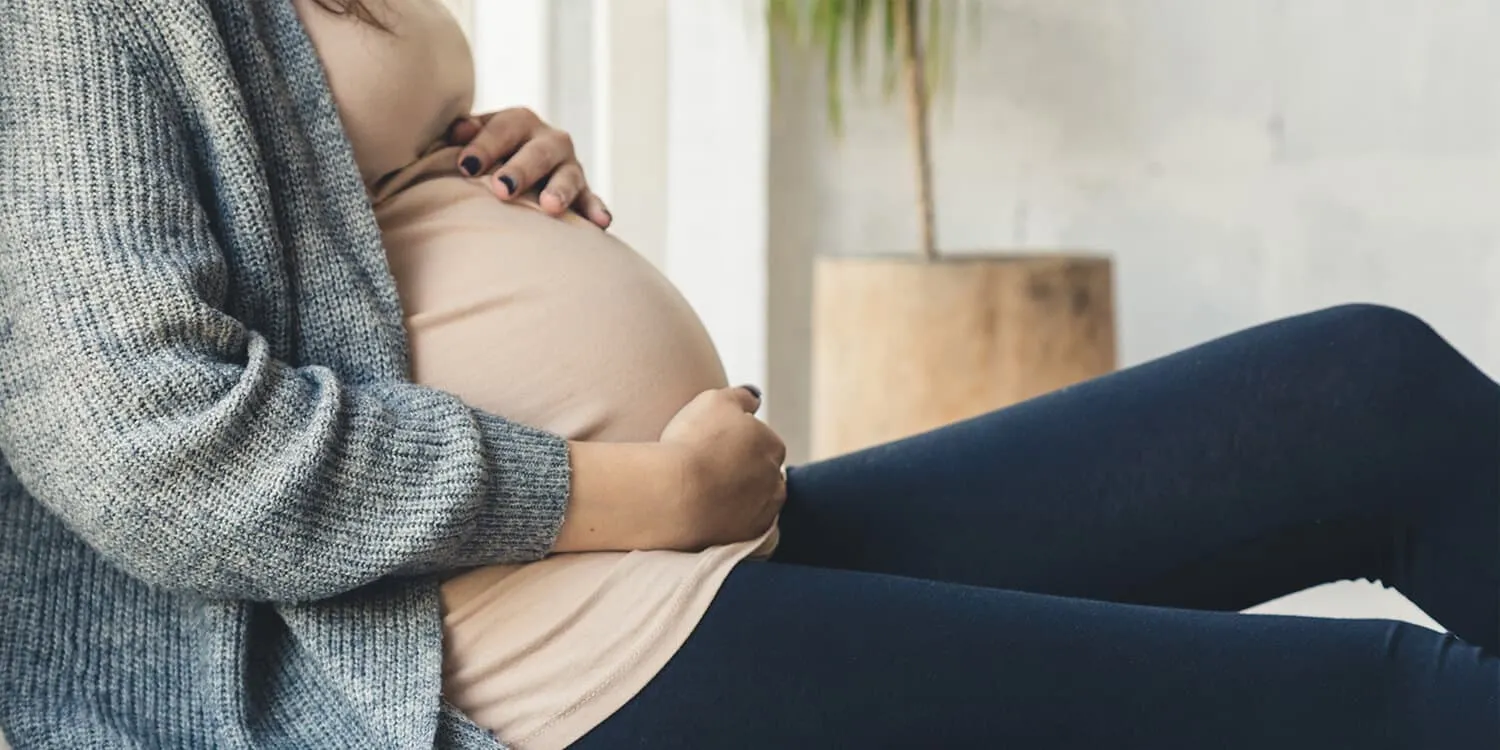 Gravid kvinne sitter på et teppe på gulvet og holder på babymagen.