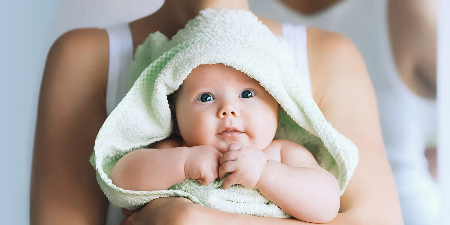 Mutter umarmt ihr Baby nach dem Bad, Baby ist in Handtuch gewickelt