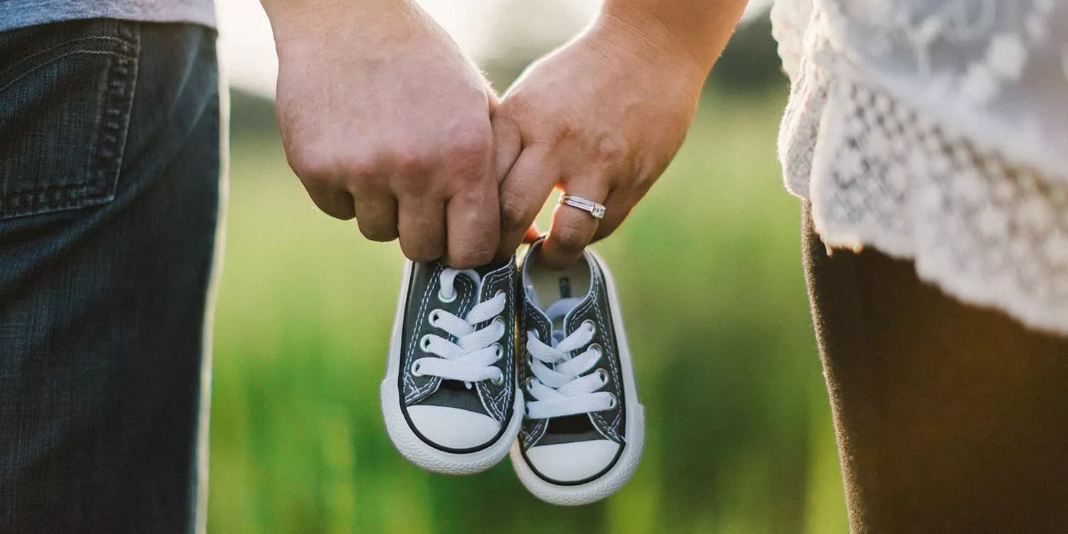 Expectant couple hold baby shoes in their hands together.