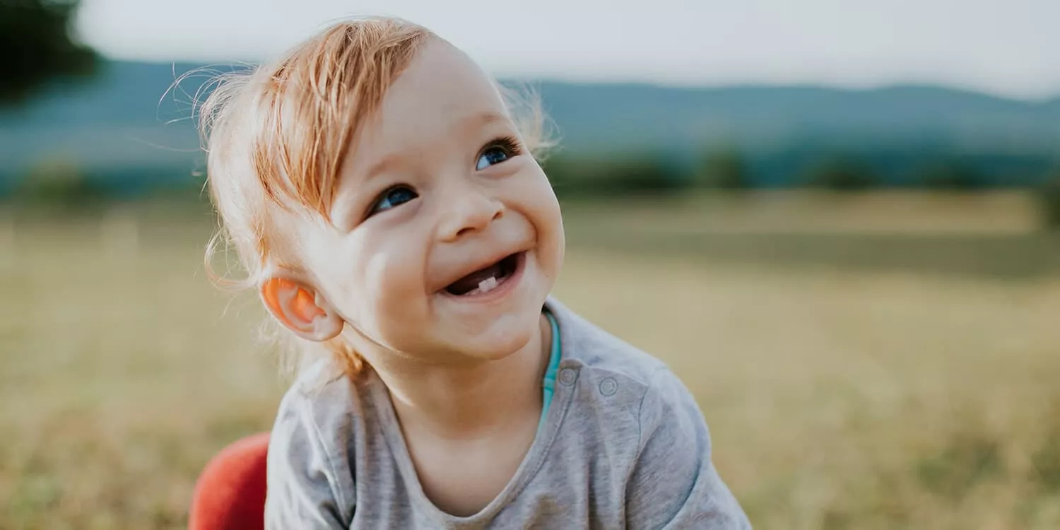 Baby kniet im Feld und lächelt, erste Zähne sind sichtbar