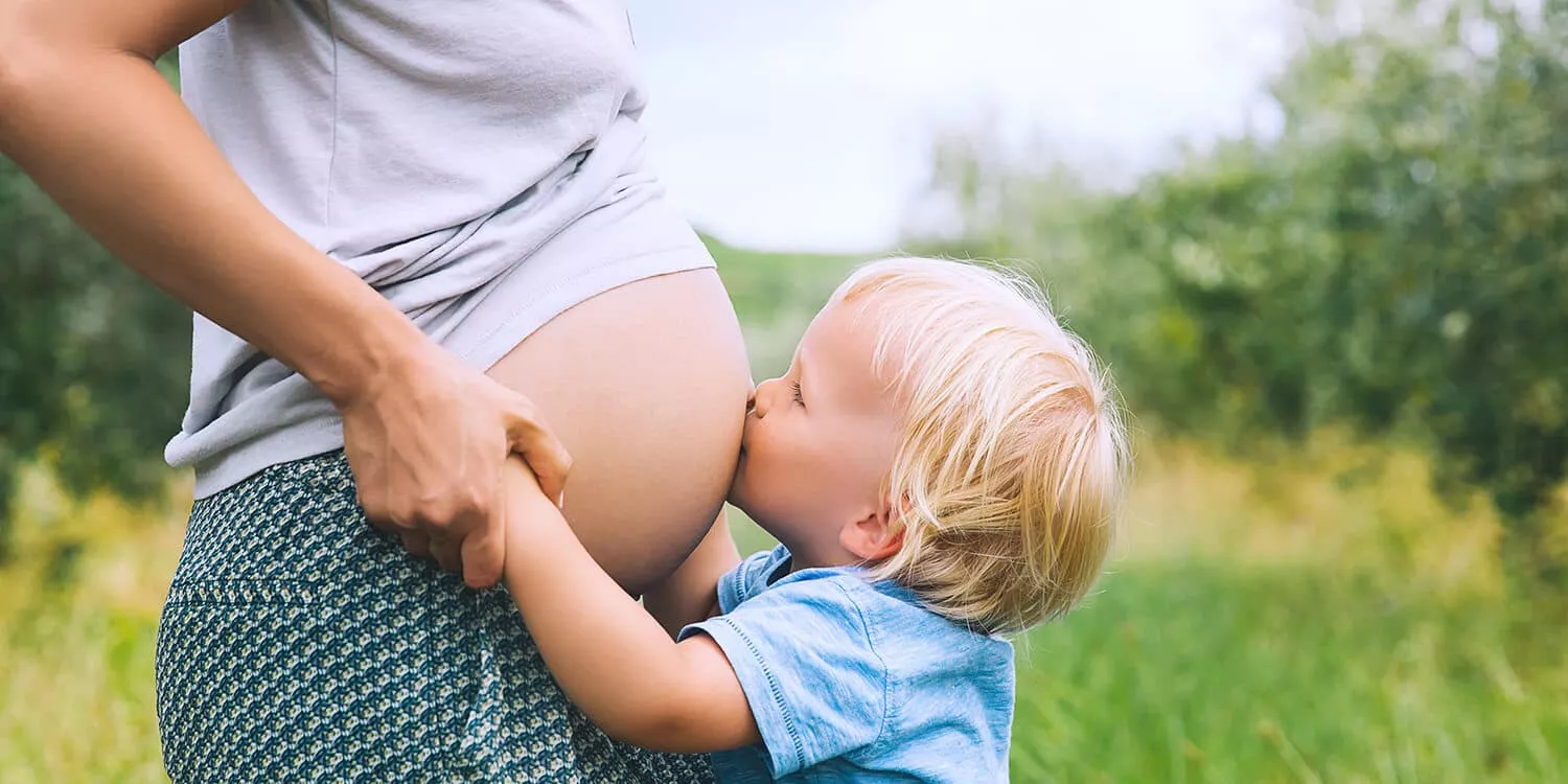 Uma criança pequena beija a barriga nua da mãe grávida 