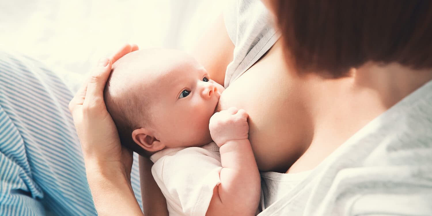 Mother breastfeeds her baby and affectionately holds its head