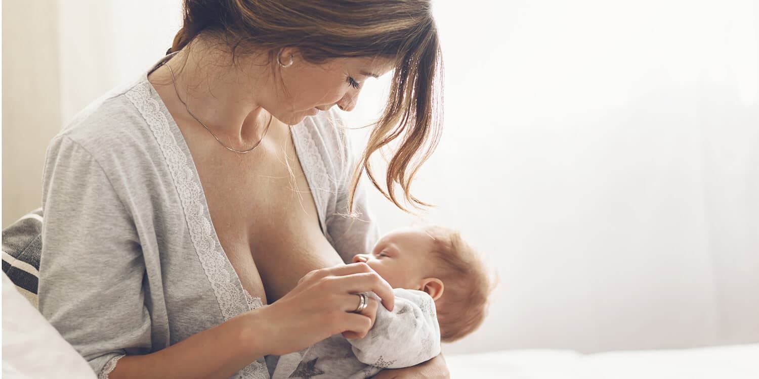 Young mother breastfeeds her baby, holds it in her arms, and smiles joyfully