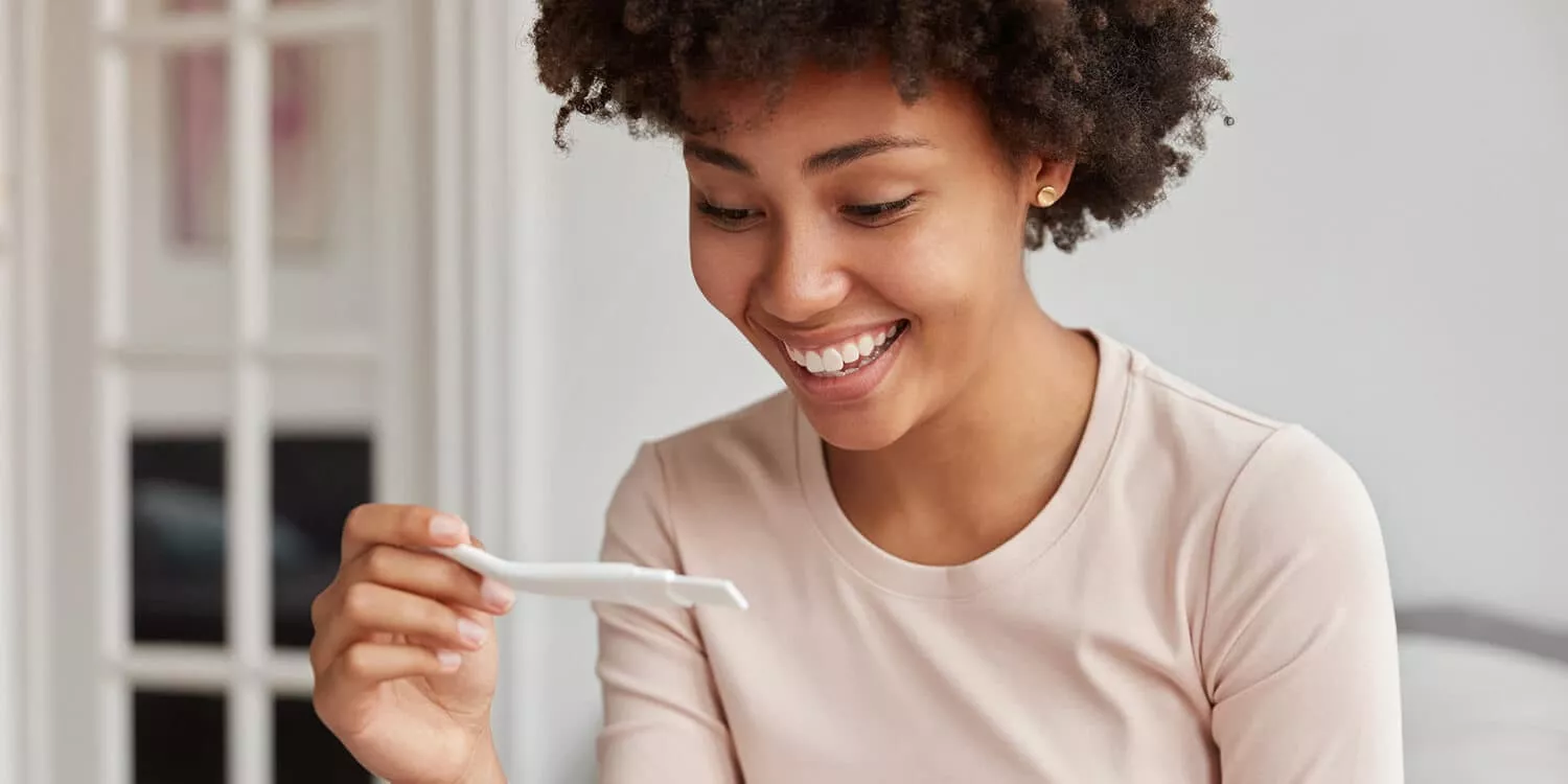 Glückliche junde Frau mit Schwangerschaftstest. 