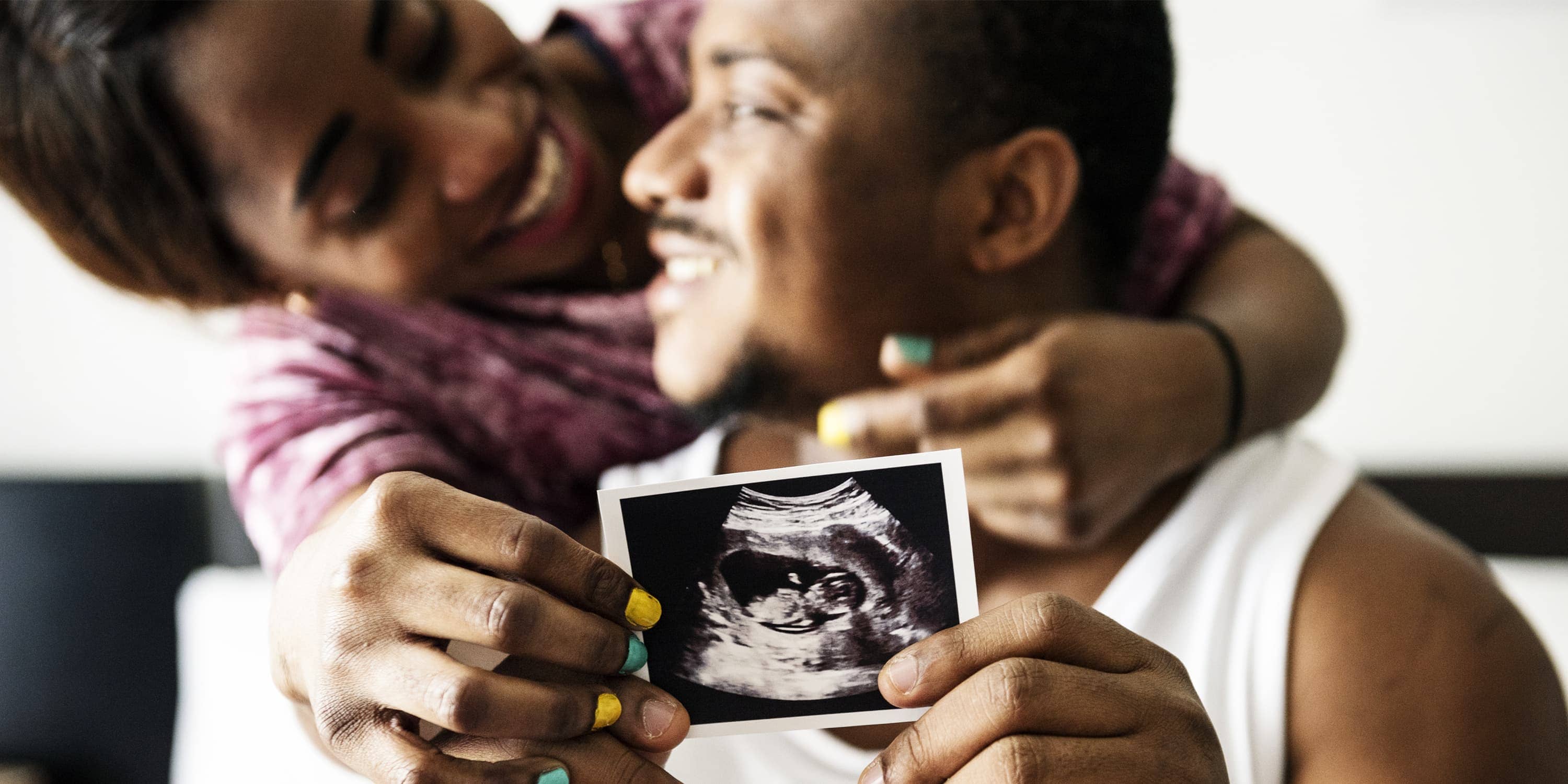 Glückliches Paar hält Ultraschallbild von ihrem Baby in die Kamera (2. Trimester)