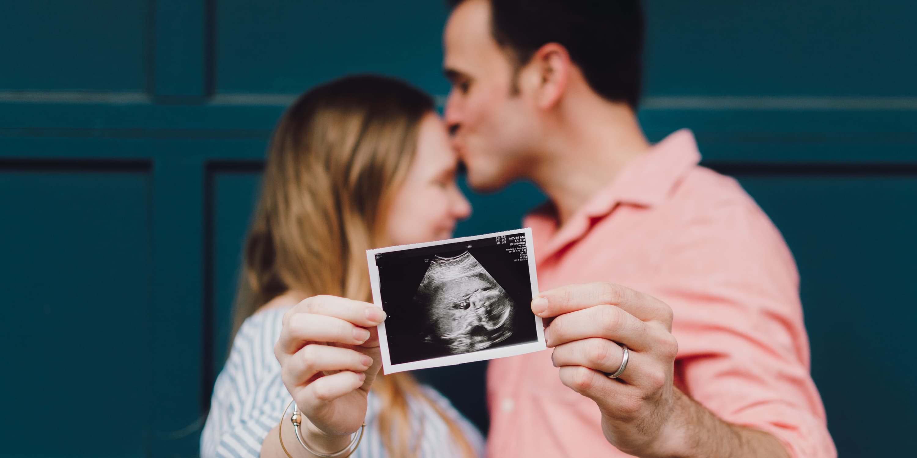 Ungt par håller upp en ultraljudsbild på bebis framför kameran.
