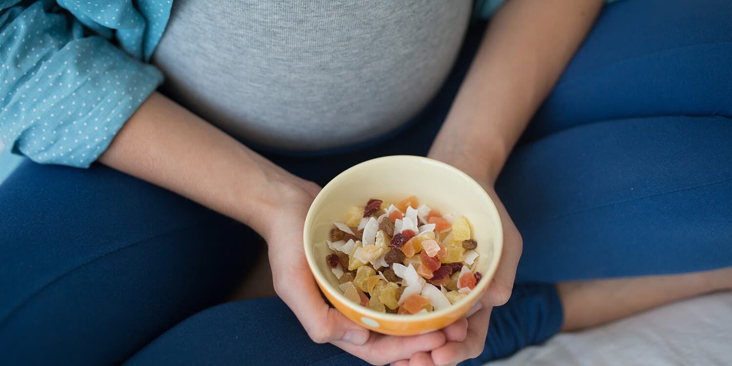Pregnant woman holds a bowl of dried fruits in front of her belly.