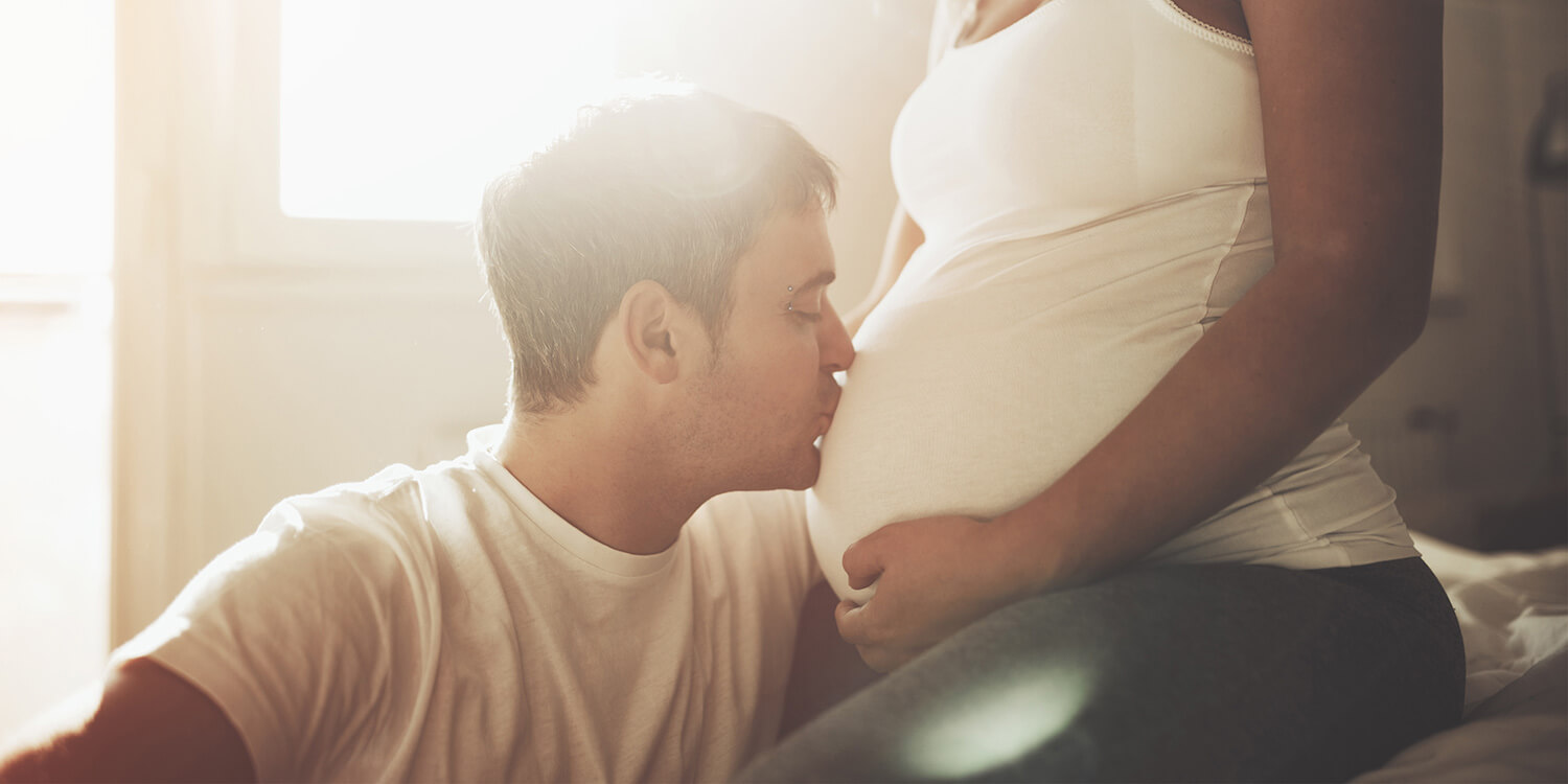 Um homem beija a barriga da mulher grávida