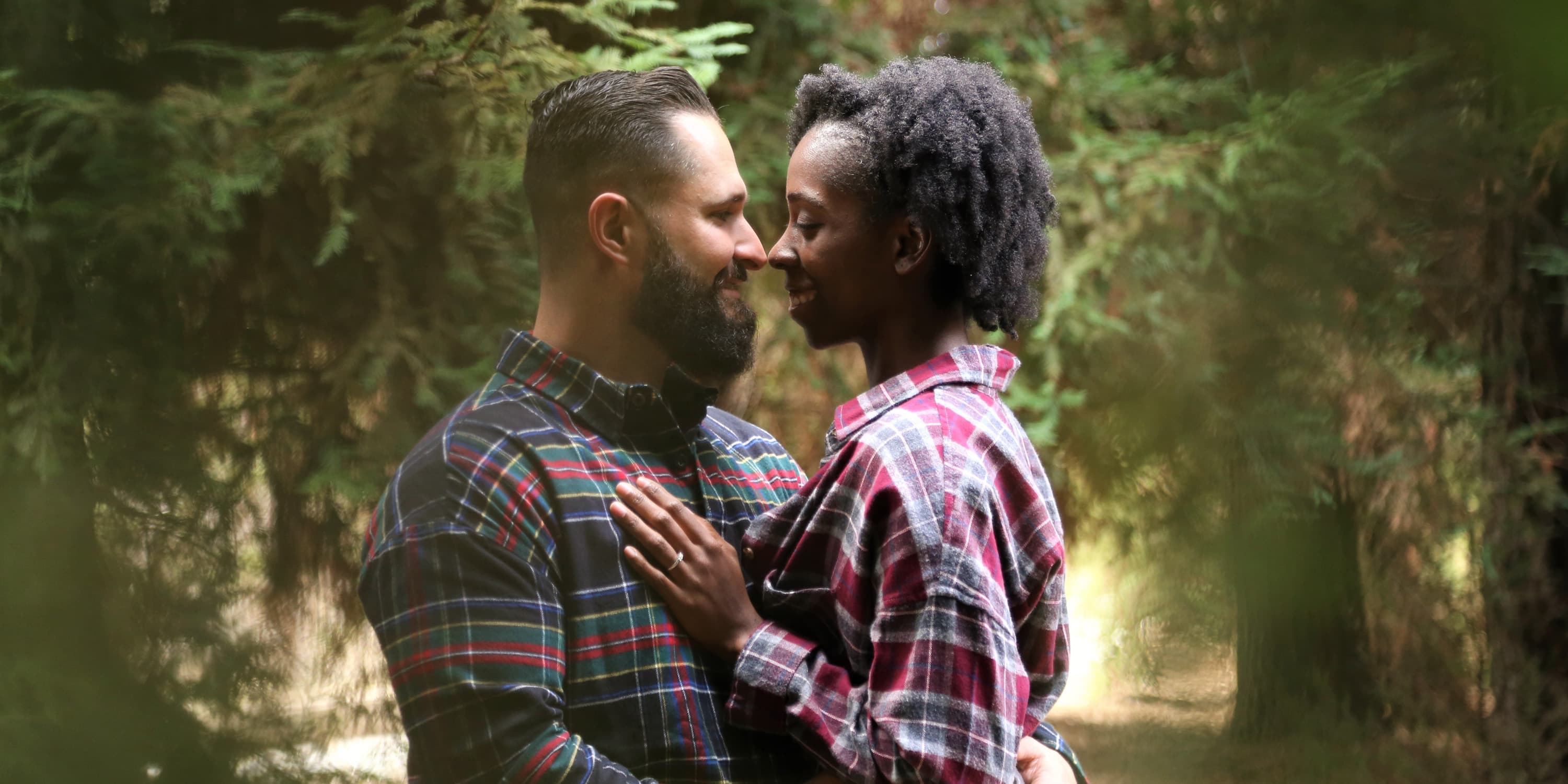 Junges Paar steht im Wald umarmt sich und lächelt sich an