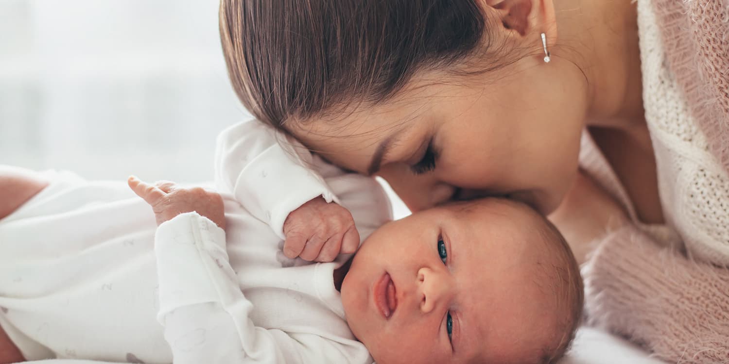 Mutter küsst Neugeborenes auf den Kopf