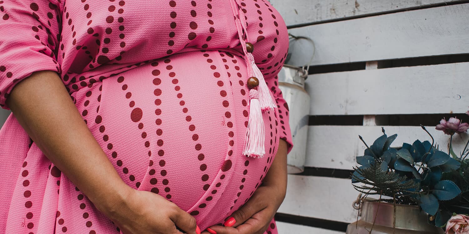 Gravid kvinde lægger armene om sin gravide mave