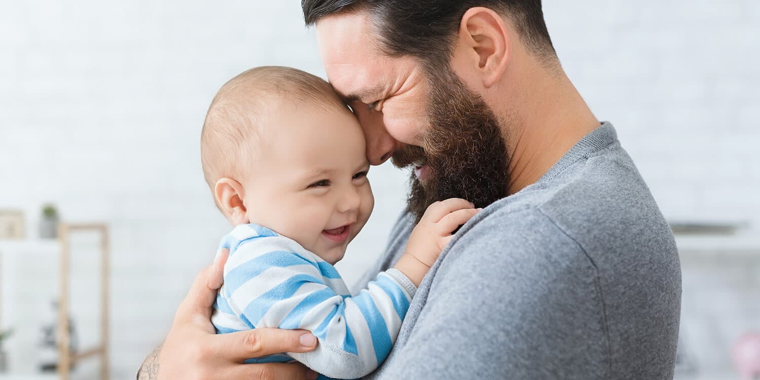 Happy father holds his laughing baby in his arms and touches his  forehead.