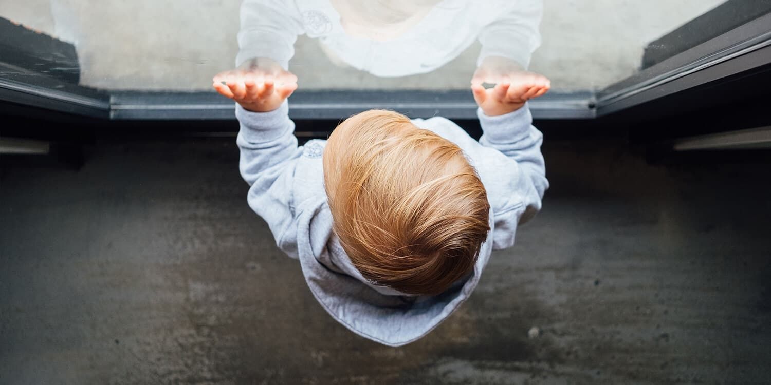 Toddler stands in front of the window pane and presses its hands against the glass