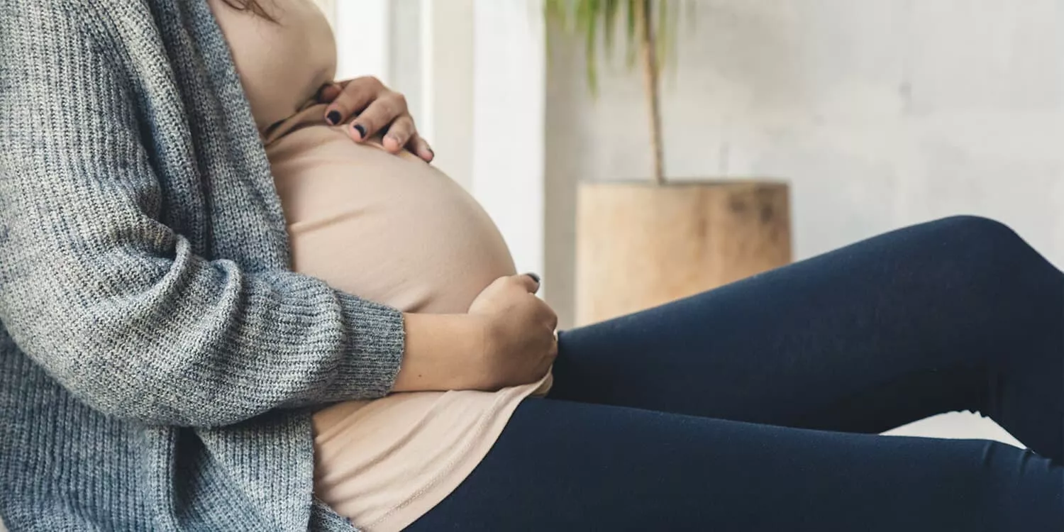 Pregnant woman sitting on the floor with her hands around her baby bump.