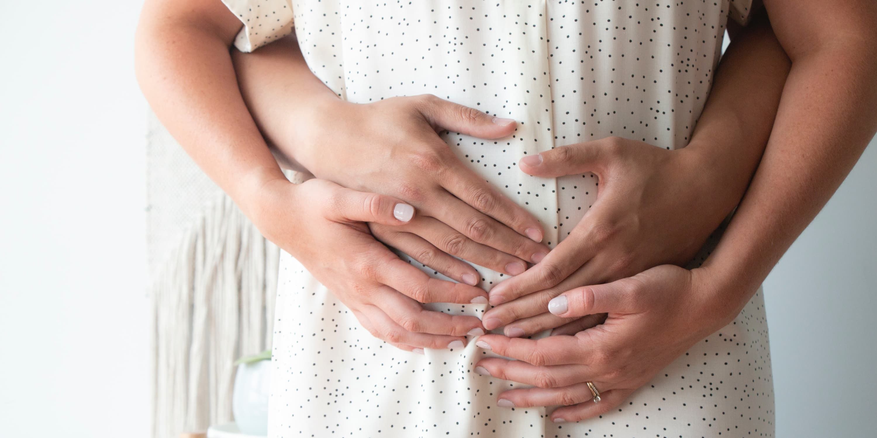 homem abraça mulher por trás na barriga, mulher coloca as mãos sobre as dele