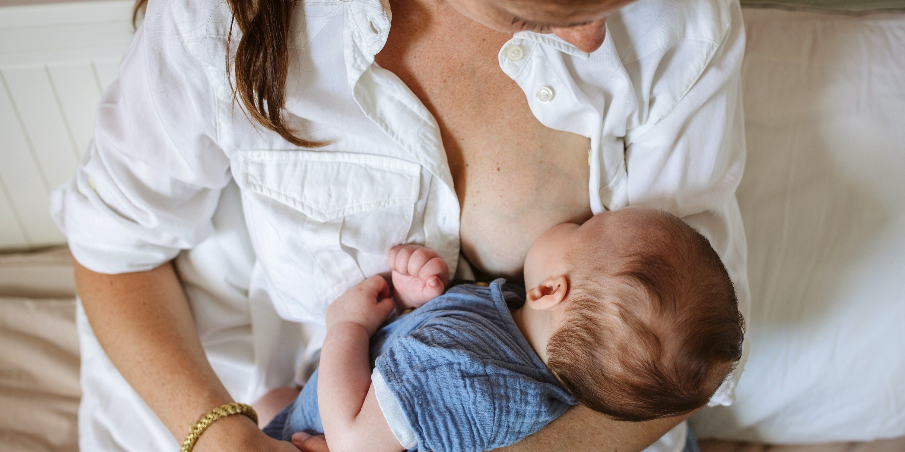 Mother is sitting on a hospital bed nursing her newborn baby. 