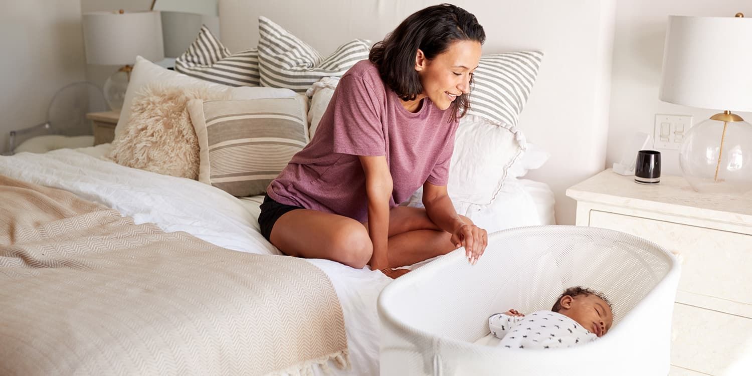 Mother lovingly looks into baby bed where her baby sleeps